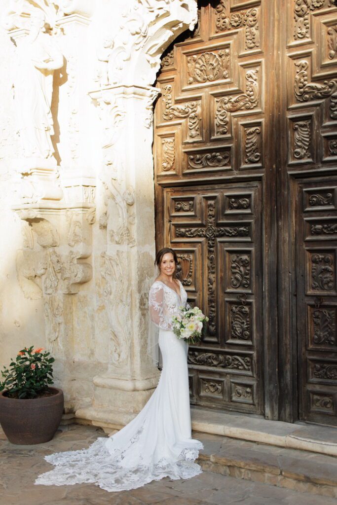 Timeless bridal portrait featuring a bride in a fitted gown with train, standing in front of carved wooden doors at a historic wedding venue.