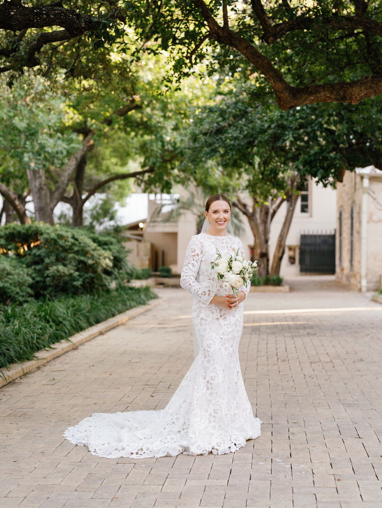 Bridal portrait of a bride in a lace gown holding a bouquet under a canopy of trees in downtown San Antonio, planned by Lila Lane Events, a Texas-based wedding planner.