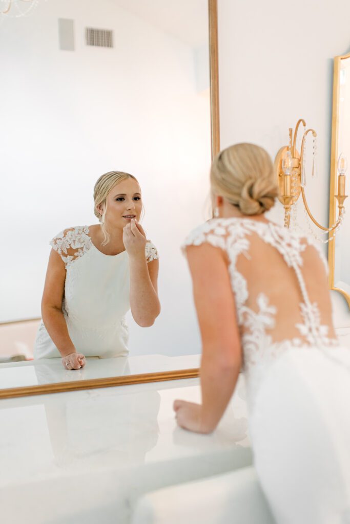 Bride applying lipstick in front of a mirror before bridal portraits, preparing her wedding day look with guidance from a Hill Country wedding planner.