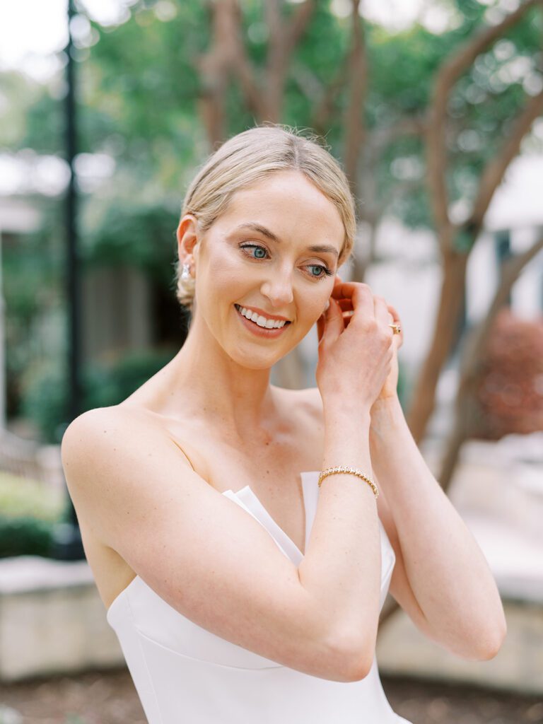 Bride putting on earrings during bridal portraits in the Texas Hill Country, getting ready with help from her wedding planner for a stress-free celebration.