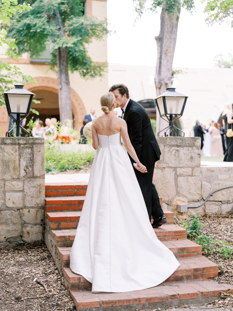 Bride and groom share a kiss on stone steps at a Central Texas venue, designed by a Hill Country wedding planner.