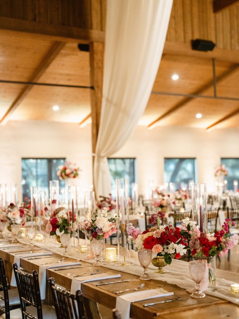 Indoor reception at The Chandelier of Gruene with draped fabric and red floral centerpieces.