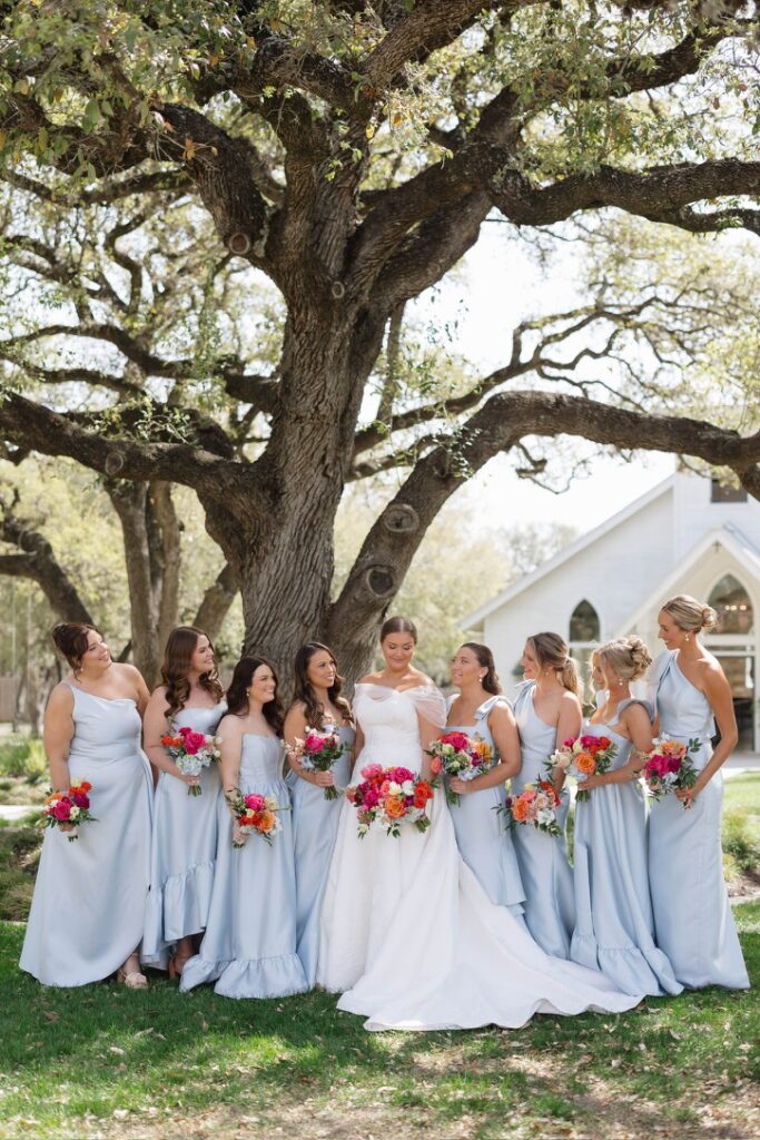 Bride with bridesmaids under oak tree at The Chandelier of Gruene, a Hill Country wedding venue.