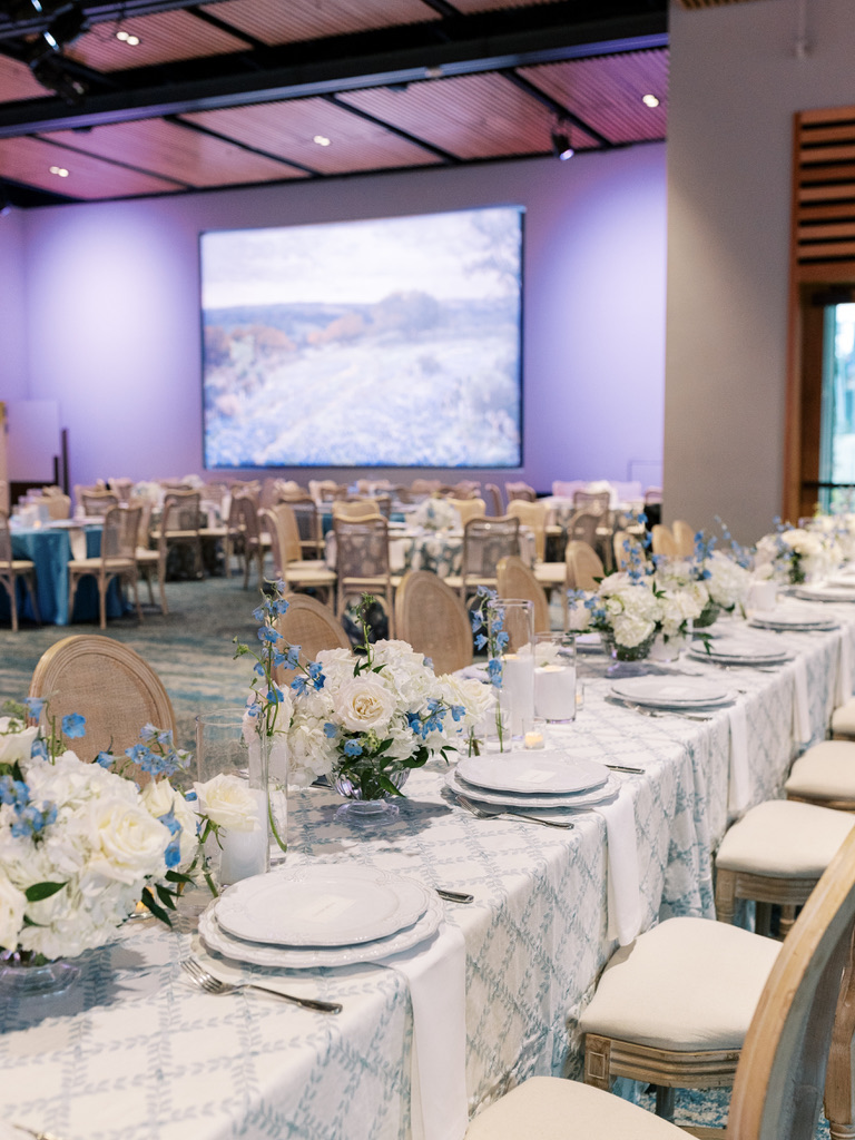 Elegant indoor wedding reception with blue uplighting and long tables at a Central Texas wedding venue.