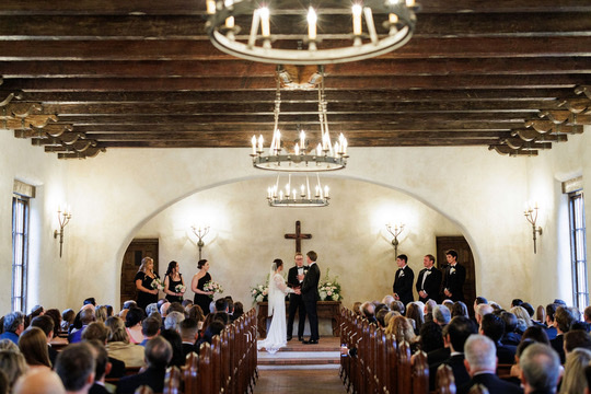 Indoor wedding ceremony in chapel with wood beams and chandeliers at Lost Mission, a Central Texas wedding venue.