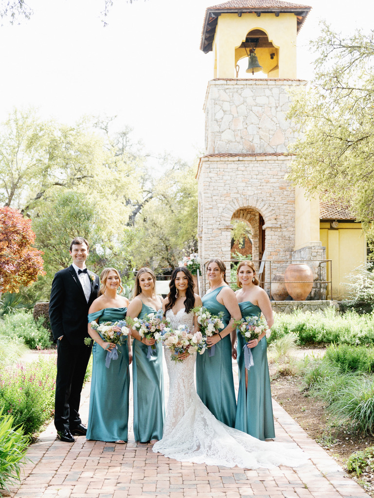 Bride, groom, and wedding party pose in front of Camp Lucy chapel at a Central Texas wedding venue.