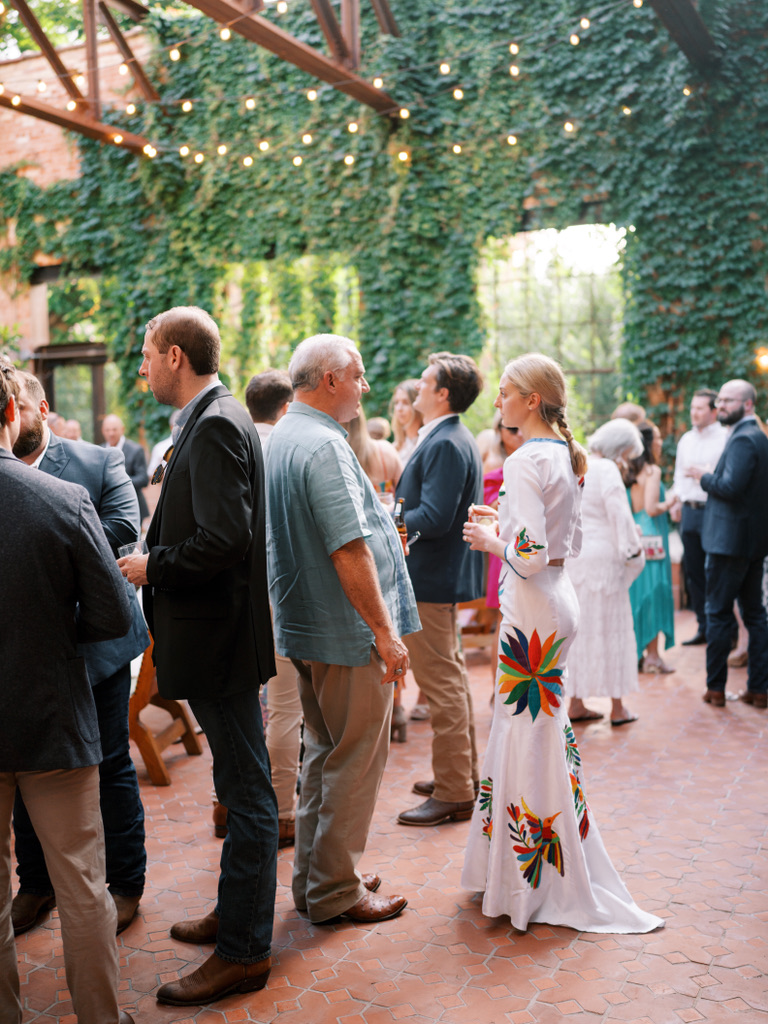 Wedding guests enjoying cocktail hour beneath string lights at a Central Texas wedding venue.