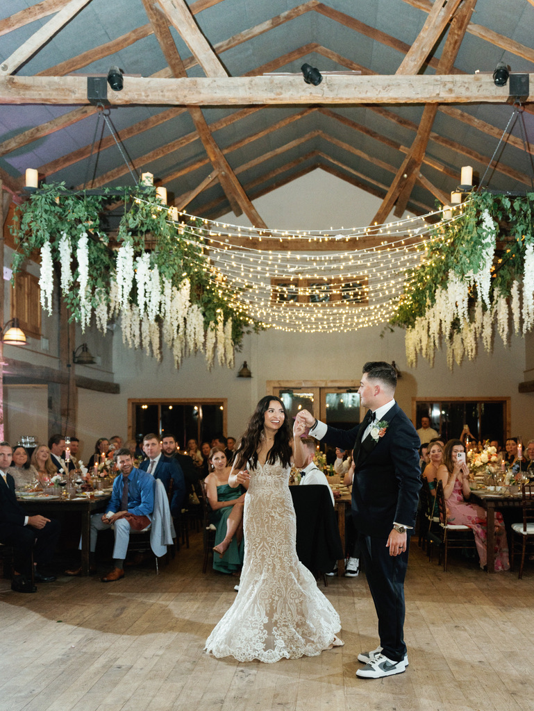 Bride and groom first dance under hanging greenery and string lights at Camp Lucy, a Hill Country wedding venue.