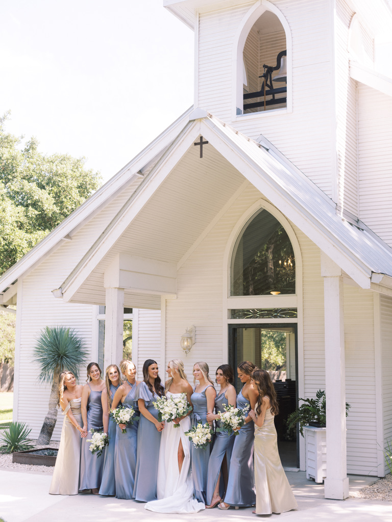 Bride and bridesmaids outside the white chapel at The Chandelier of Gruene, a Central Texas wedding venue.