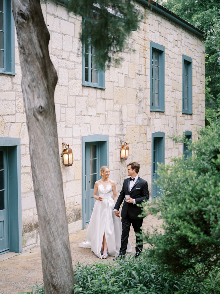 Bride and groom walking near stone building at a Central Texas wedding venue, planned by a local wedding planner.