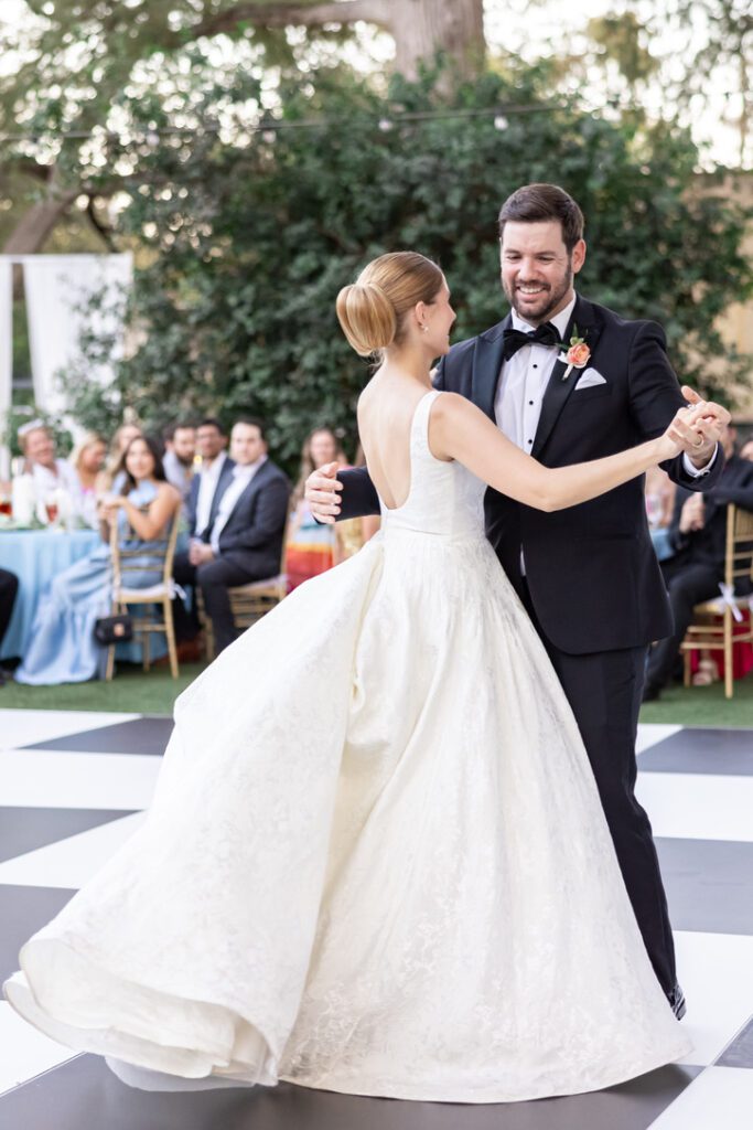 Bride and groom first dance on black and white checkered floor at an outdoor Central Texas wedding venue.