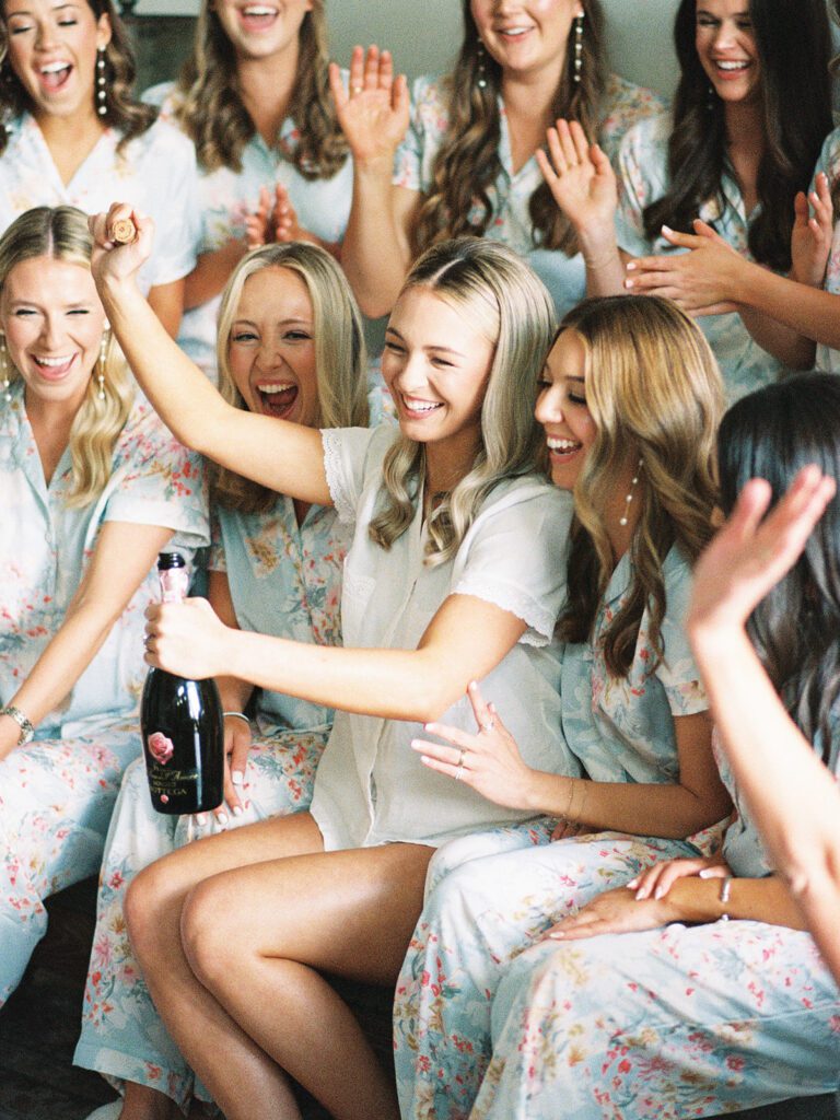 Bridesmaids cheering as bride pops champagne | Joyful pre-ceremony celebration planned by San Antonio wedding planner