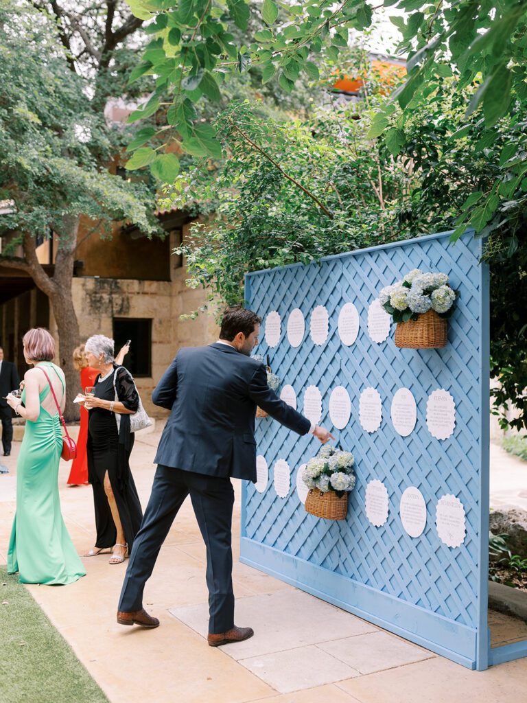 Guest interacting with blue escort card wall display during cocktail hour | Creative timeline touch by Austin wedding planner Lila Lane Events