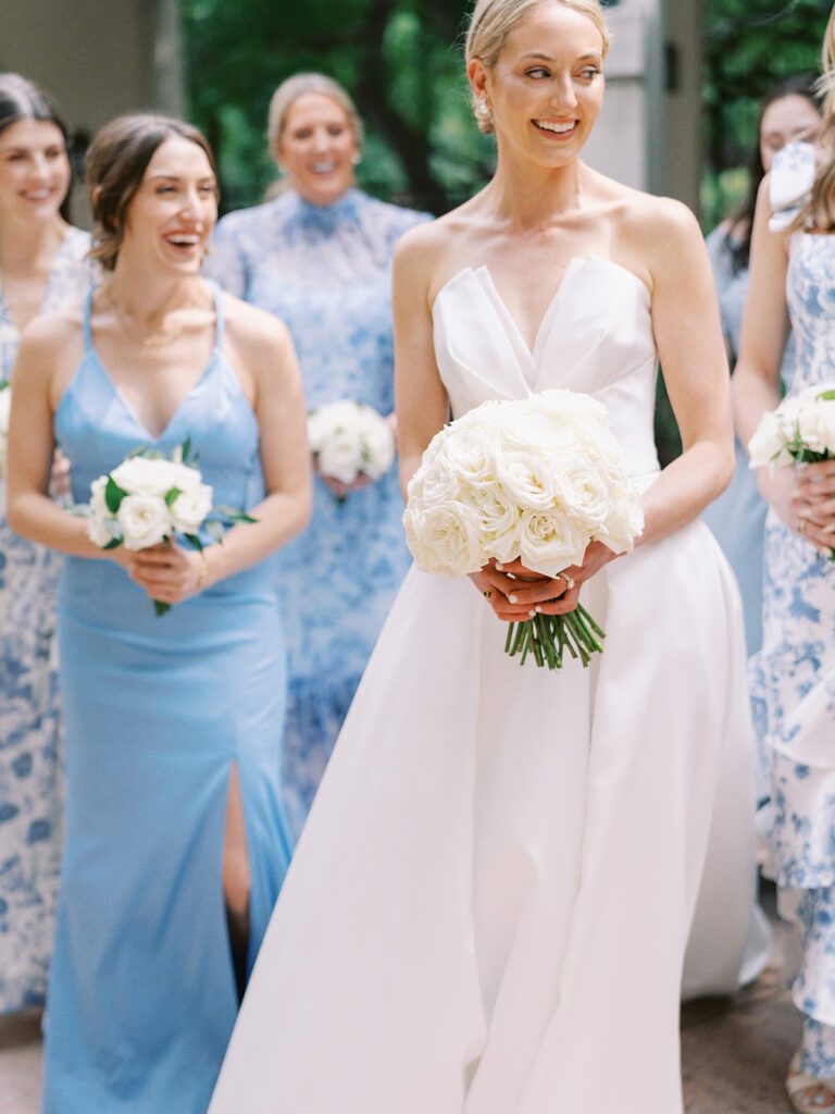 Bride in modern white gown holding cream rose bouquet with her bridal party | Joyful pre-ceremony timeline moment by San Antonio planner