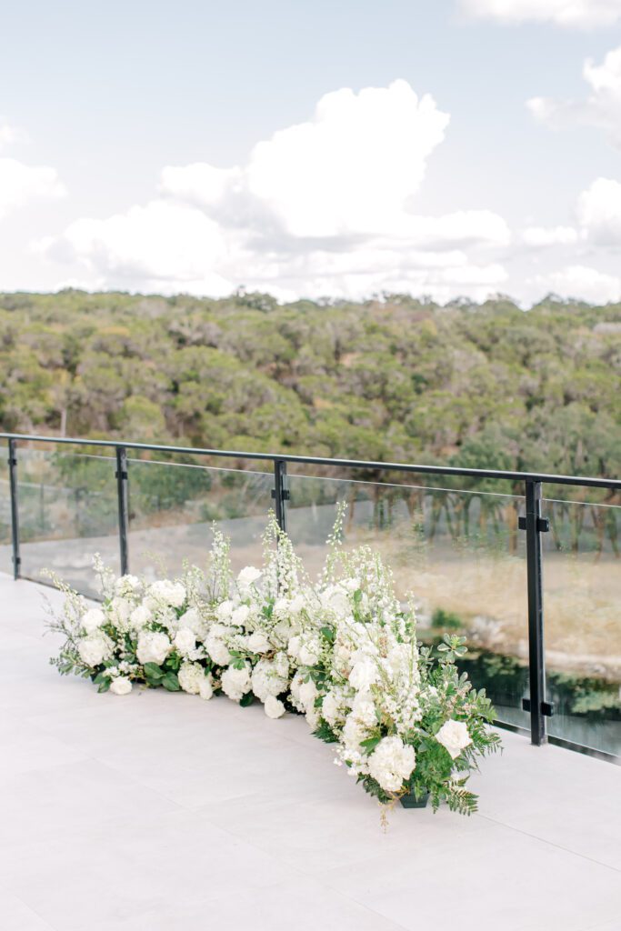 White floral arrangements lining the glass balcony at The Videre Estate, overlooking scenic Hill Country views.