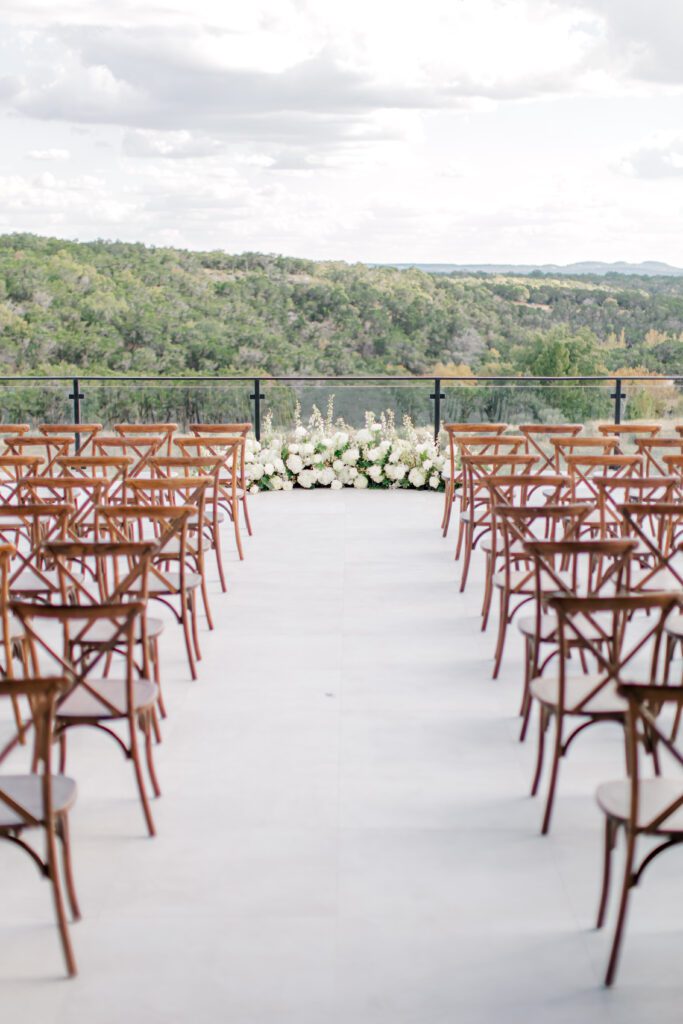 Wedding ceremony setup at The Videre Estate with wooden chairs facing lush white florals and a sweeping Hill Country backdrop.