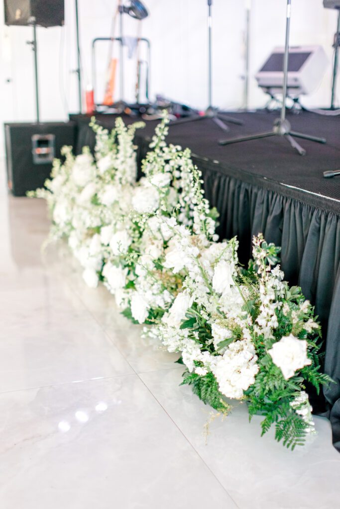Lush white floral arrangements lining the base of a stage for a wedding reception at The Videre Estate.