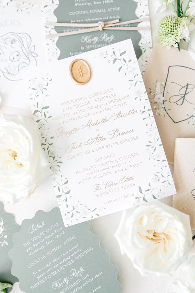 Elegant white and green wedding invitation suite with gold wax seal, floral details, and custom cocktail napkins styled with fresh roses.