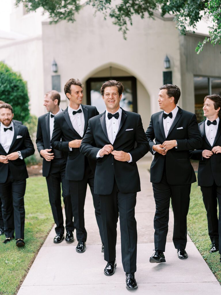 Groom and groomsmen in black tuxedos walking together before ceremony, showing how wedding party size factors into a realistic wedding budget Texas couples create.