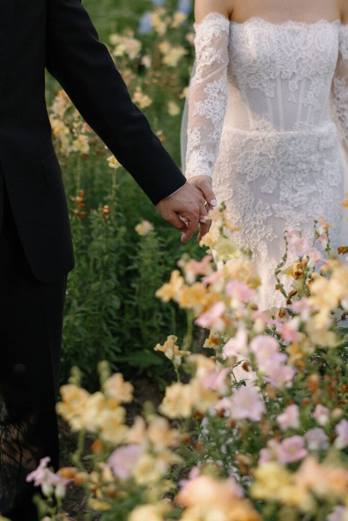 Close up of newlyweds holding hands in field of flowers, so pleased with their list of wedding vendors